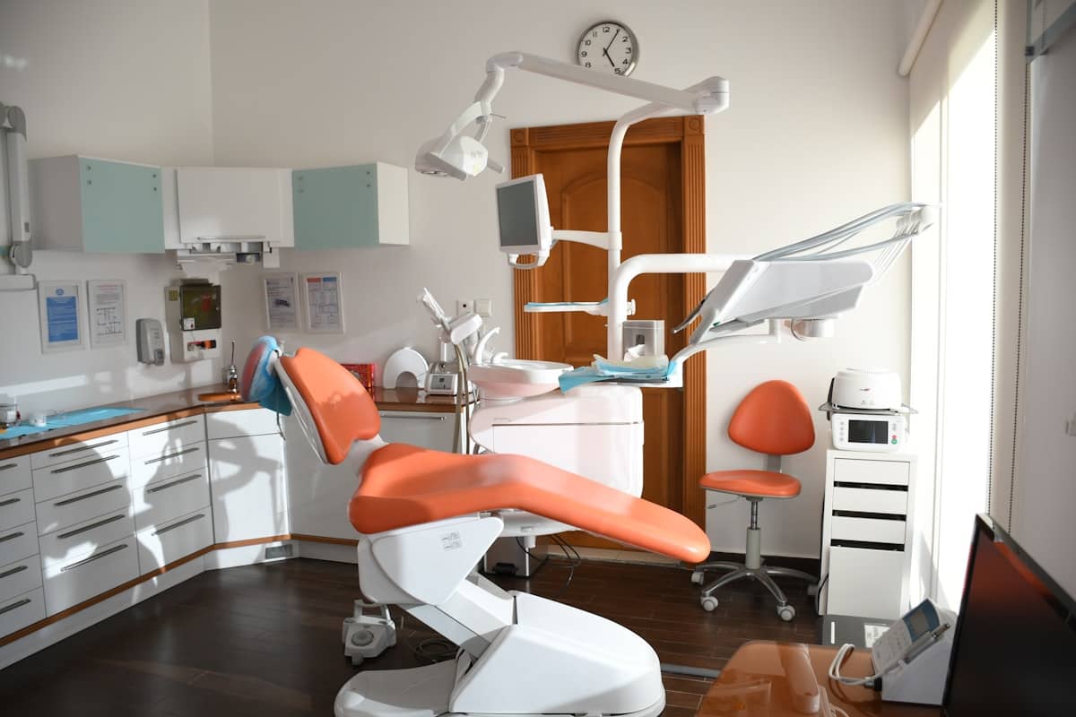 Sunlit dental operatory with a coral chair, wood floor, and a big bright window