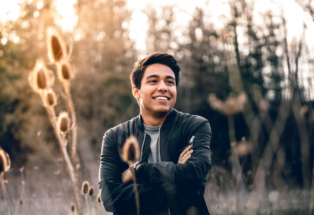 Young man smiling in a golden-hour field, arms crossed and at ease