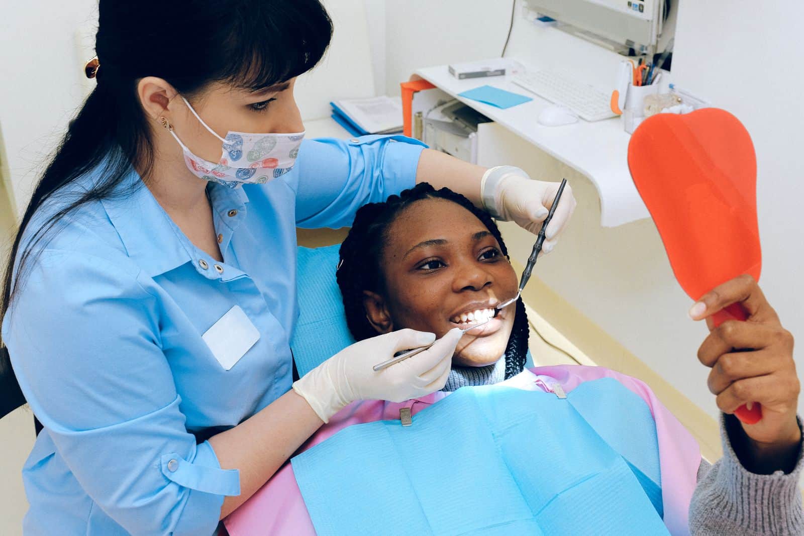 Hygienist chatting with a patient who checks her smile in a coral hand mirror