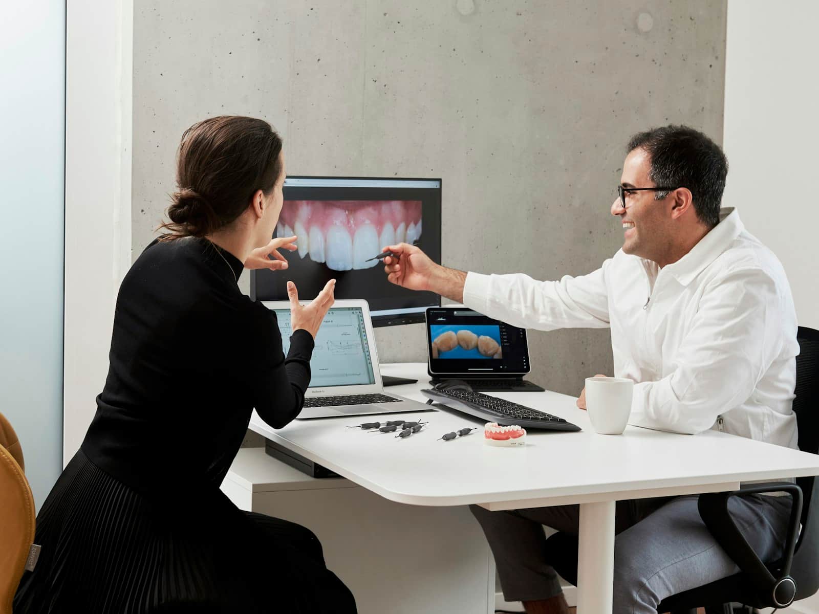 Dentist walking a patient through her dental scan on a screen, tooth model on the desk