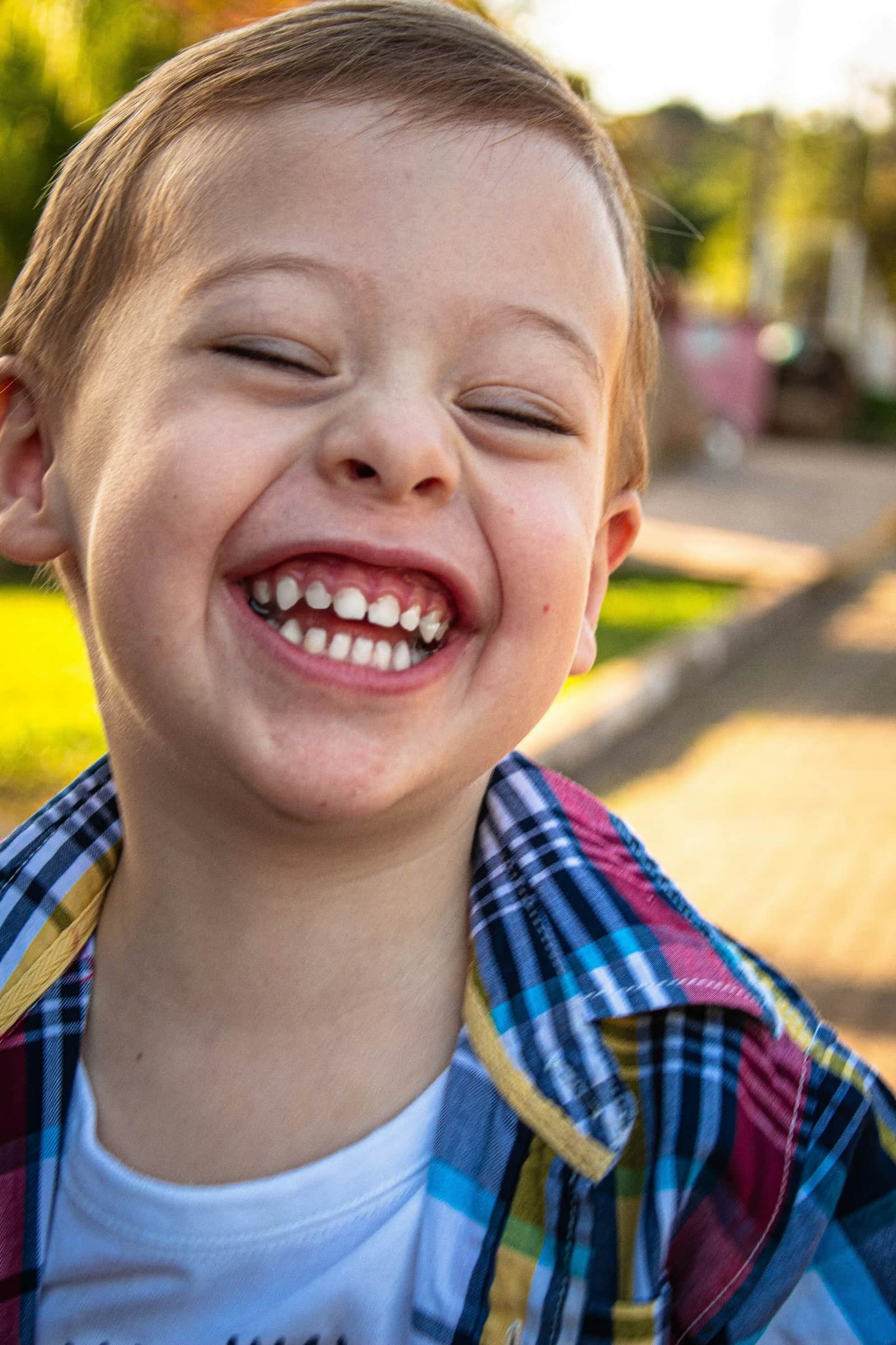 Young boy laughing hard in warm golden light, showing off a big kid grin