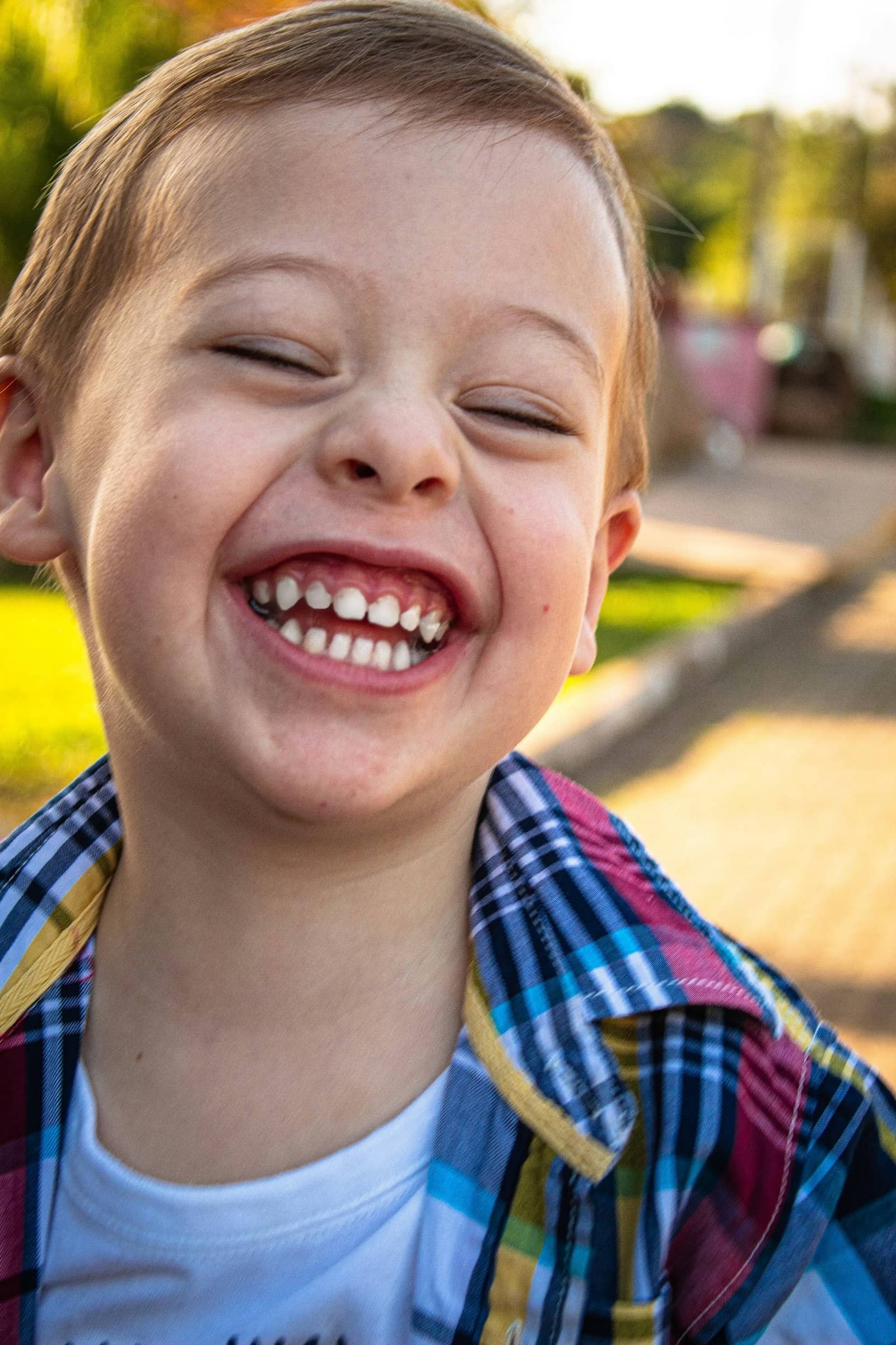 Young boy laughing hard in warm golden light, showing off a big kid grin